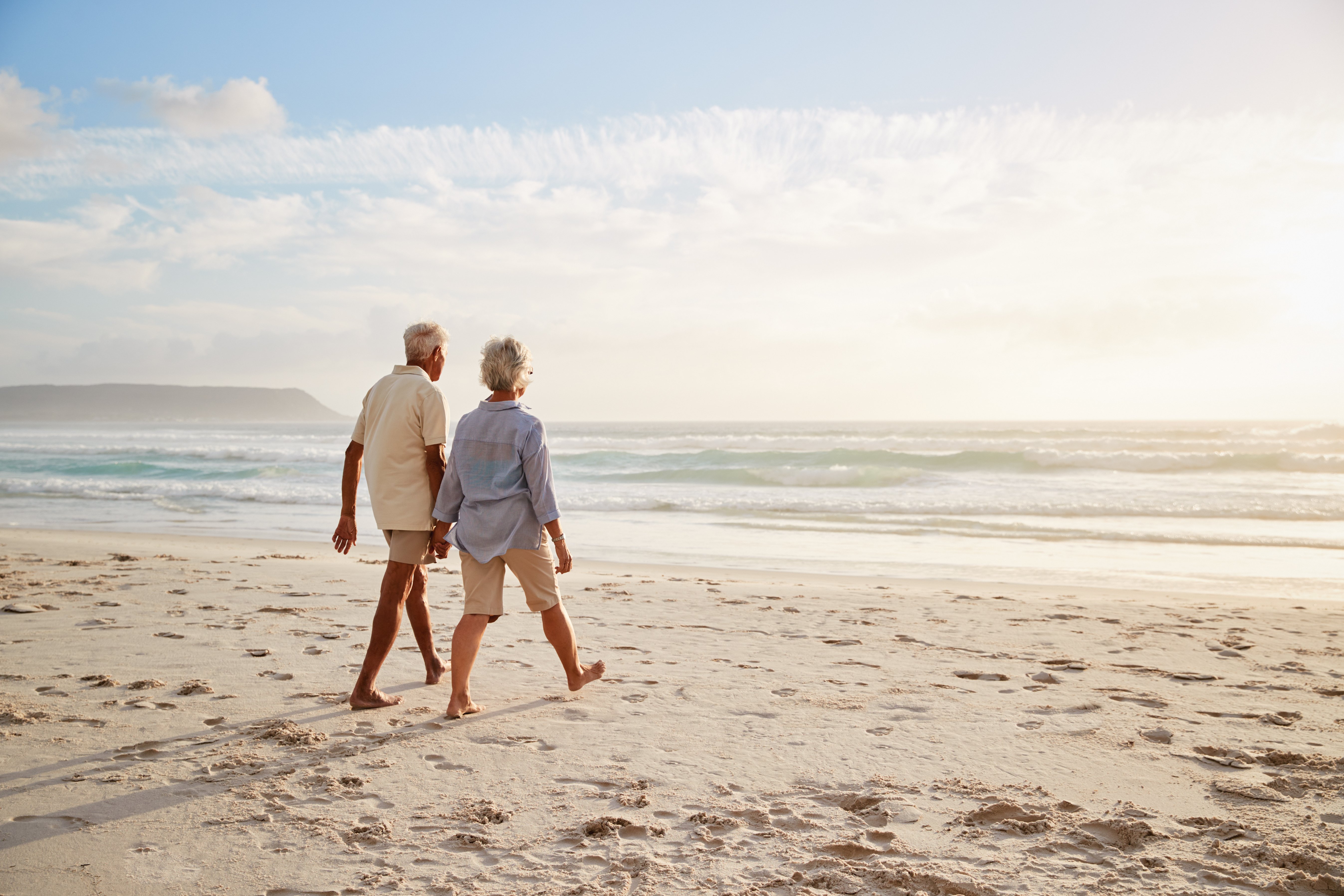 Senior couple enjoying a beach walk after transitioning away from active property management