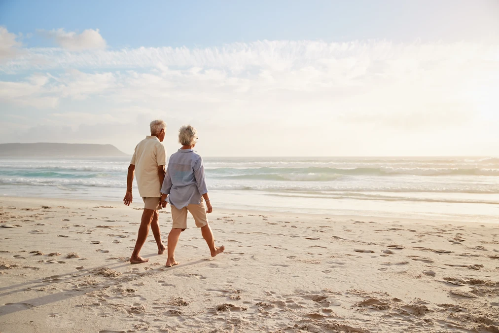 Senior couple enjoying a beach walk after transitioning away from active property management